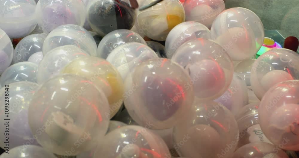 Claw crane attempting to pick up a prize inside a transparent round capsule. The claw is moving down, trying to grab the prize Claw crane attempting to pick up a prize inside a transparent round capsule. The claw is moving down, trying to grab the prize