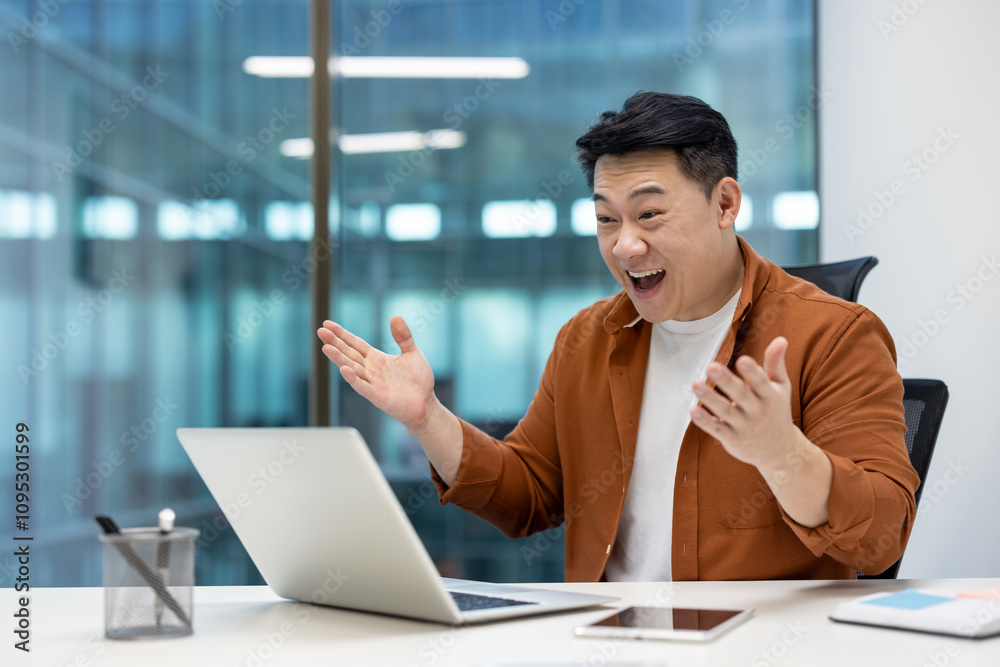 Asian man businessman with bright smile in modern office using laptop, expressing excitement and success during video call. Achieving goals, enhancing productivity with innovative collaboration tools. Asian man businessman with bright smile in modern office using laptop, expressing excitement and success during video call. Achieving goals, enhancing productivity with innovative collaboration tools.