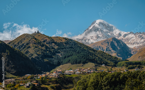 Gergeti Trinity Church perched on a hill with the snow-covered Mount Kazbek towering in the background, under a vibrant blue sky in Georgia