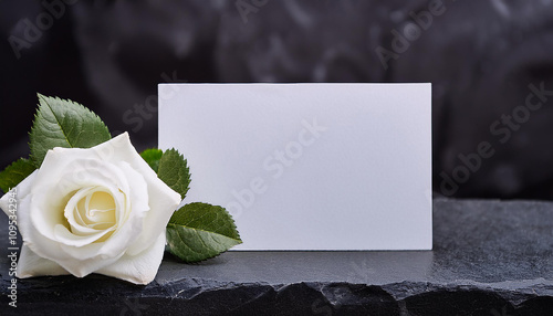 Condolence card and white flower on dark stone surface. Mock-up. Close-up.