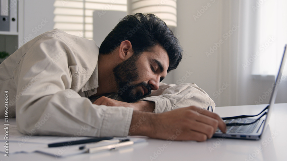 Lazy weary sleepy male manager tired exhausted Arabian Indian businessman employee working computer boring remote job man fall sleep on desktop napping in office overwork fatigue no energy sleeping