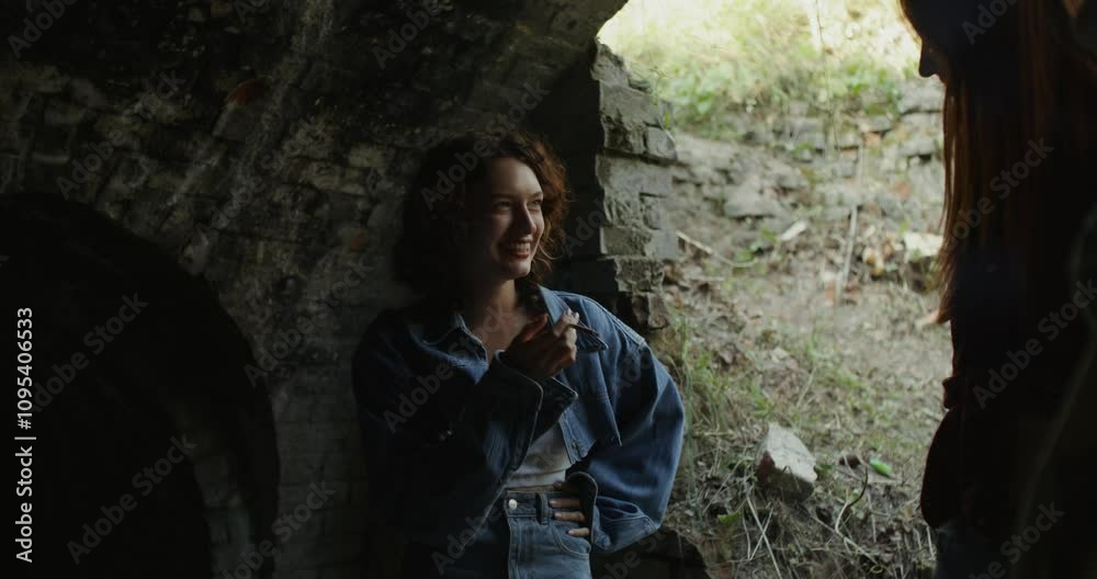 Three friends are smiling and talking standing near a ruined historical building. They smoke. A sunny summer day