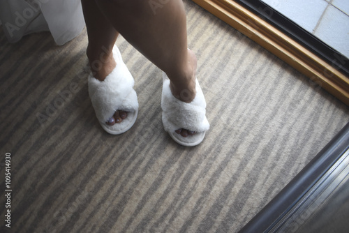 Woman's legs in beautiful white house slippers on a grey carpet