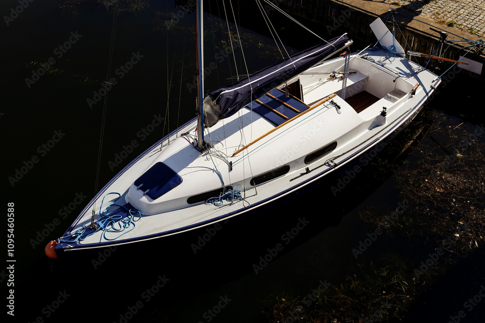 Yacht moored at marina pier. Boat tied with a rope. Sailboat docked. Top view of boat at the marina. Bow of the boat facing the water. Fastened at the dockside. Parked boat on a lake. Yacht moored at marina pier. Boat tied with a rope. Sailboat docked. Top view of boat at the marina. Bow of the boat facing the water. Fastened at the dockside. Parked boat on a lake.