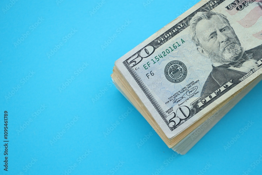 Big amount of fifty dollar bills in thick stack lies on bright blue color paper background Big amount of fifty dollar bills in thick stack lies on bright blue color paper background