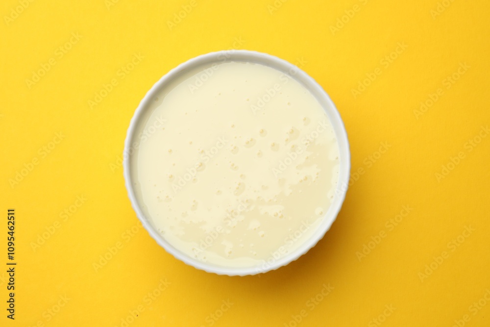 Tasty condensed milk in bowl on orange background, top view Tasty condensed milk in bowl on orange background, top view