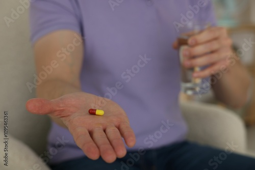 Man with pill and glass of water at home, closeup