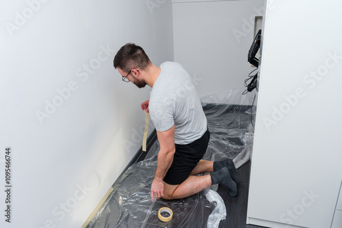 Man is kneeling on the floor in front of a wall, painting it