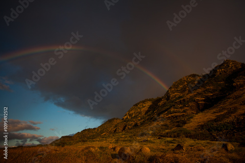 Rainbow in stormy sky over rocky mountains at sunset