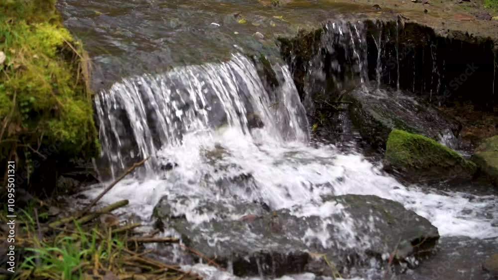 Small waterfall cascading over rocks in a serene natural setting surrounded by greenery Small waterfall cascading over rocks in a serene natural setting surrounded by greenery