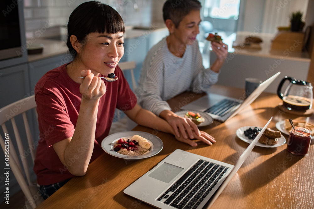 Lesbian couple using laptop on kitchen table during breakfast