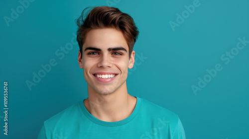 A cheerful young man in a teal shirt stands against a blue backdrop, radiating joy and positivity.