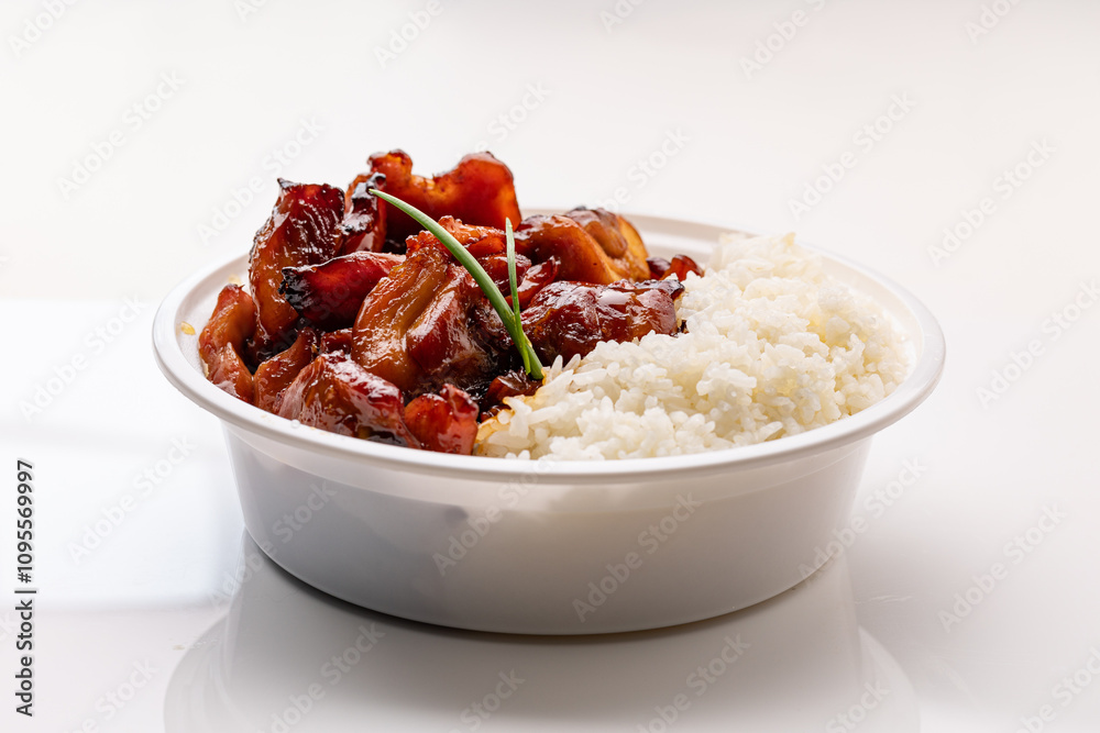 A white disposable plastic bowl filled with glazed stir-fried chicken and boiled rice, set against a white background. A white disposable plastic bowl filled with glazed stir-fried chicken and boiled rice, set against a white background.