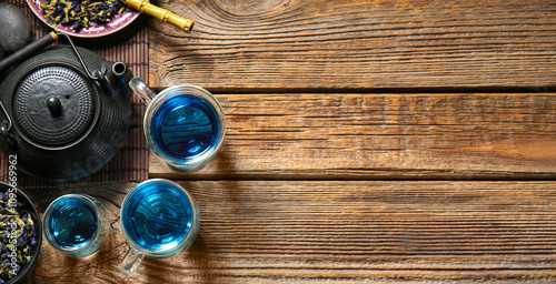 Glass cups of organic blue tea and dried flowers on wooden background photo