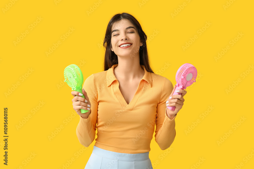 Young woman with mini fans on yellow background Young woman with mini fans on yellow background