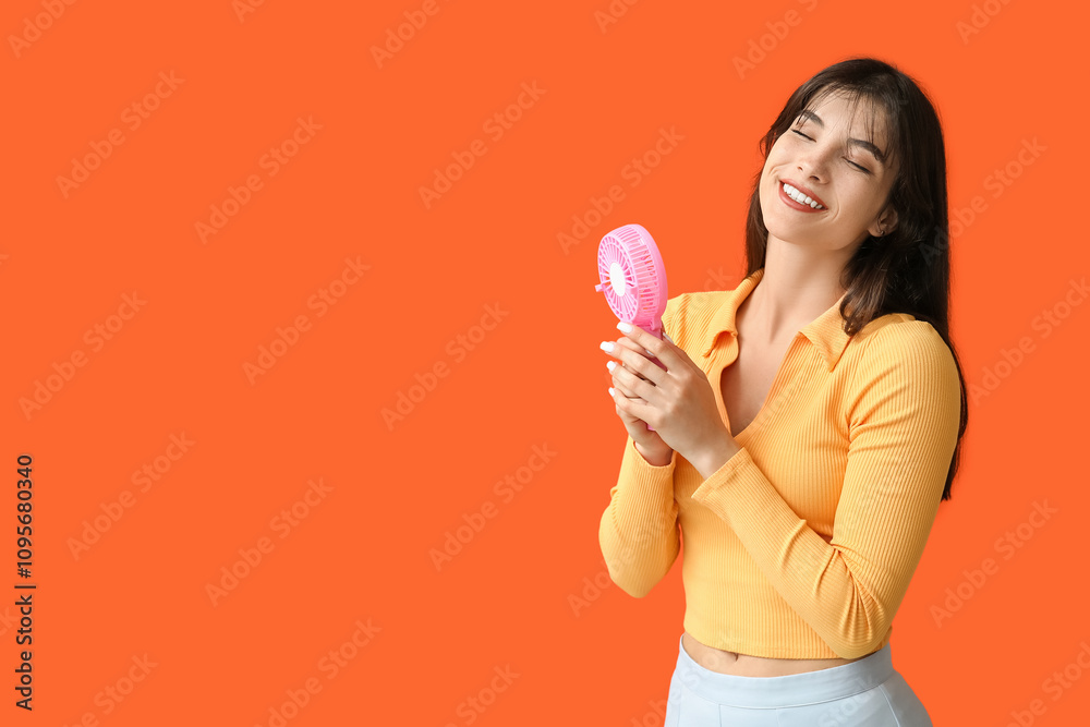Young woman with mini fan on orange background Young woman with mini fan on orange background