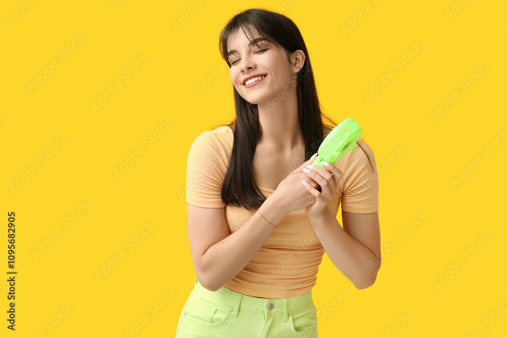 Young woman with mini fan on yellow background Young woman with mini fan on yellow background
