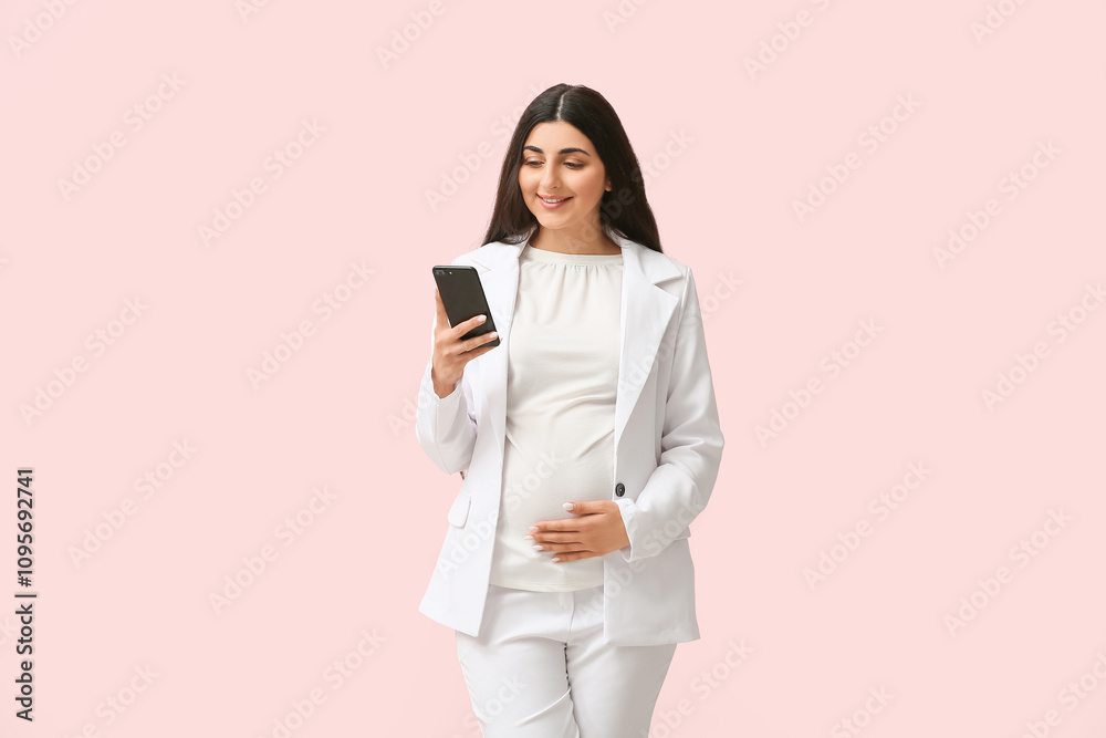 Beautiful pregnant businesswoman using mobile phone on pink background Beautiful pregnant businesswoman using mobile phone on pink background