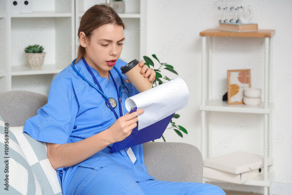 Young female medical student with clipboard drinking coffee on sofa at home Young female medical student with clipboard drinking coffee on sofa at home