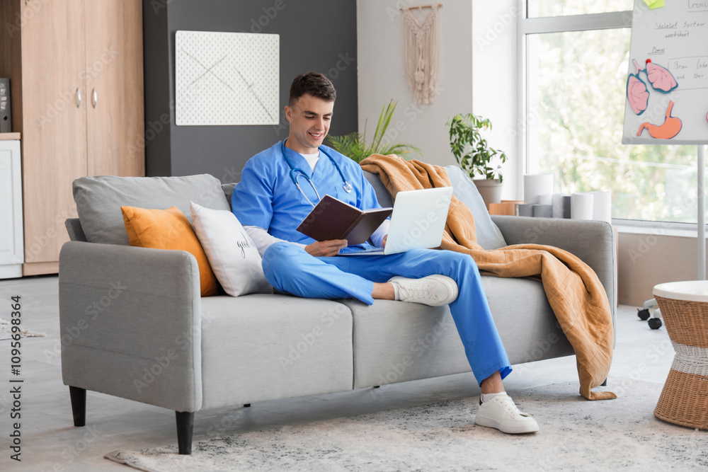 Male medical student studying with book and laptop on sofa at home Male medical student studying with book and laptop on sofa at home