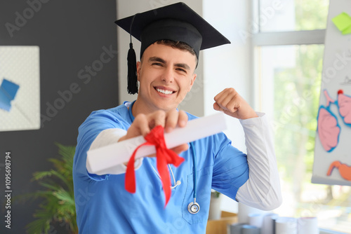 Male medical student in graduation hat holding diploma at home