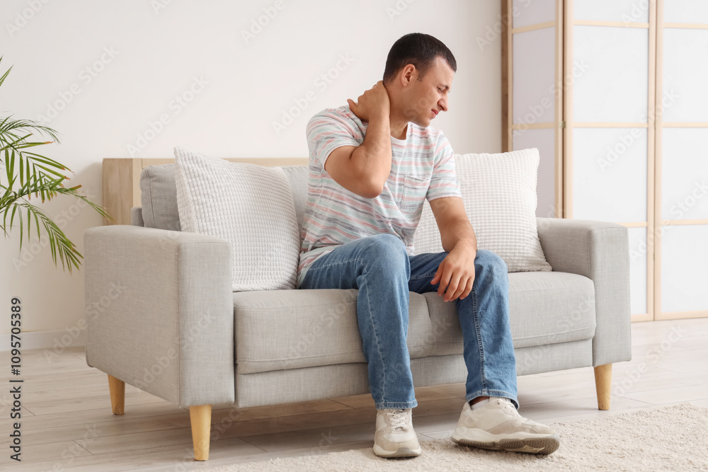 Young man suffering from pain in his neck on sofa at home Young man suffering from pain in his neck on sofa at home