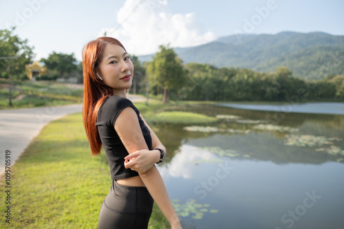 A woman stands in front of a lake, wearing a black shirt and black pants