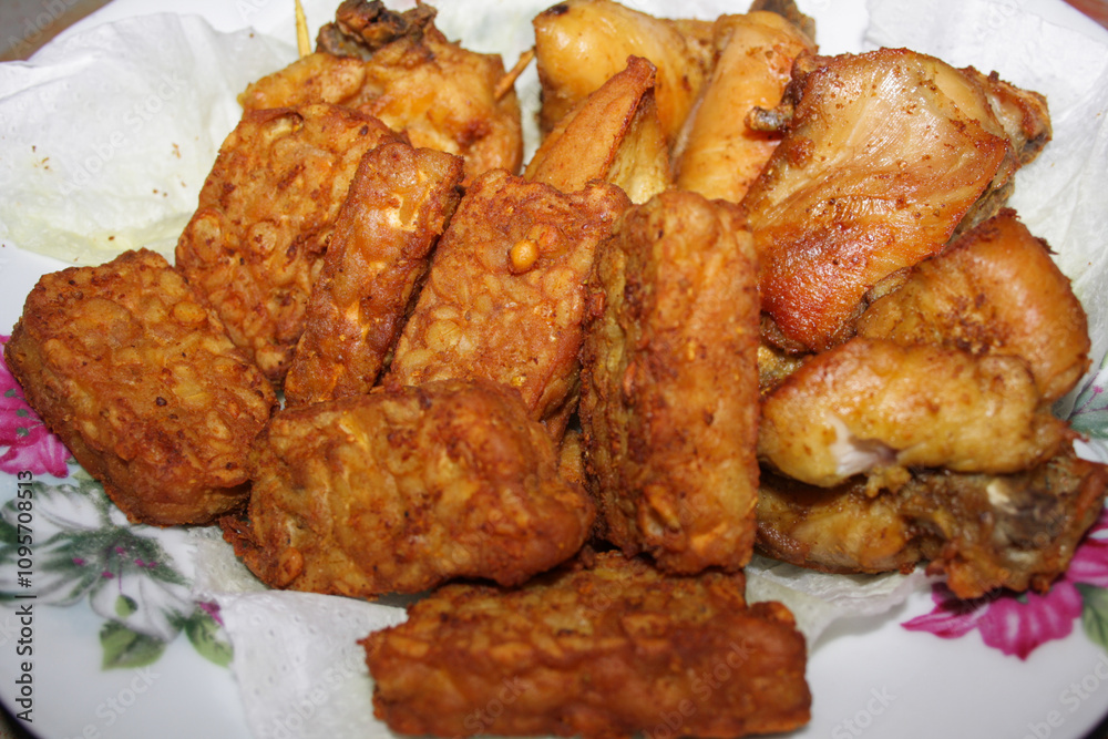 Photo of fried chicken and tempeh on a white plate, traditional Indonesian food Photo of fried chicken and tempeh on a white plate, traditional Indonesian food