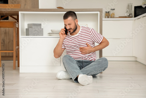 Young man suffering from heart attack and talking with mobile phone in kitchen