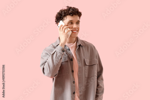 Handsome young man talking by mobile phone on pink background