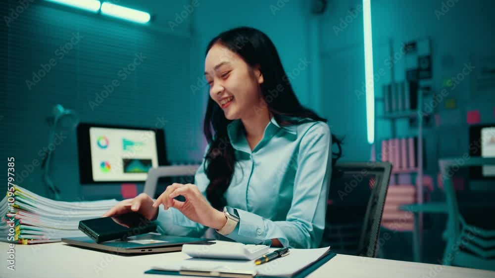 Young accountant is smiling while paying online with a credit card on her smartphone. She is sitting at her desk in her office Young accountant is smiling while paying online with a credit card on her smartphone. She is sitting at her desk in her office
