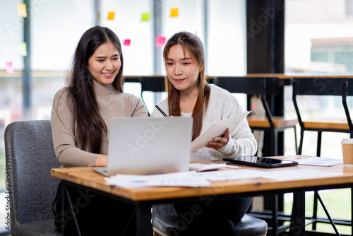 Two asian confident business people point to graphs and charts to analyze market data, balance sheet, account, net profit to plan new sales strategies to increase production capacity. 