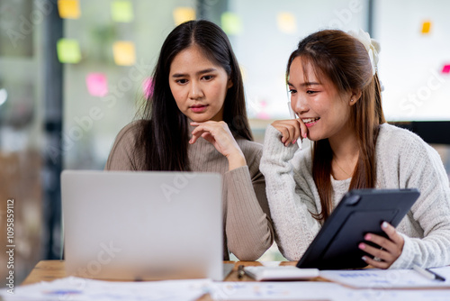 Two asian confident business people point to graphs and charts to analyze market data, balance sheet, account, net profit to plan new sales strategies to increase production capacity. 