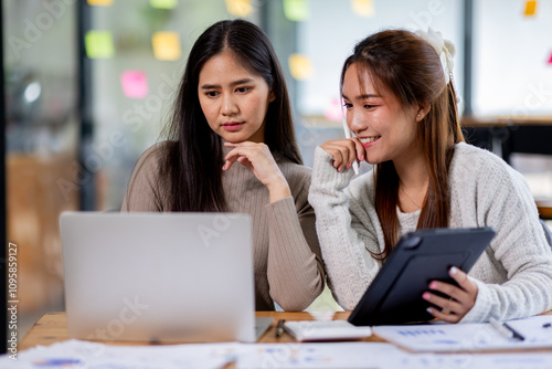 Two asian confident business people point to graphs and charts to analyze market data, balance sheet, account, net profit to plan new sales strategies to increase production capacity.	
