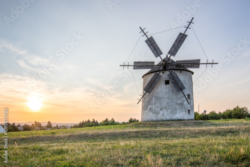 Windmill with wooden wings in a landscape setting. Fields, meadows and flowers appear in the sunset. Landscape shot in nature with a mill. historically untypical for the Balaton region in Hungary