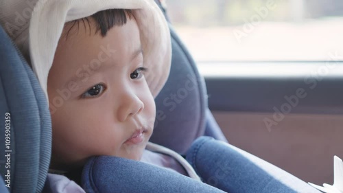 Close-up of Asian child boy in a car seat wearing a sunhat, captured in a reflective and calm moment.