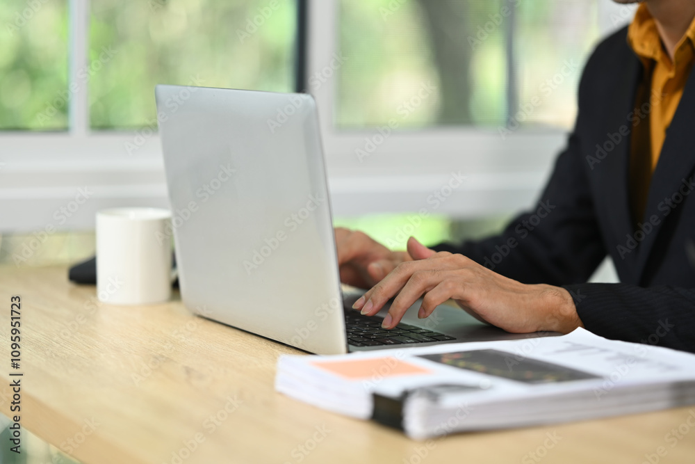 Close up of businessman working on a laptop in modern office with natural light streaming through window Close up of businessman working on a laptop in modern office with natural light streaming through window