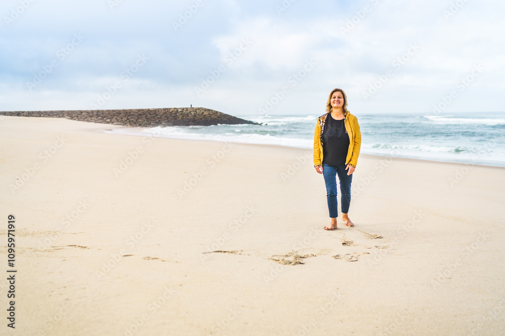 A woman with bare feet, smiling, stands on the shore of the Atlantic Ocean near the pier; an empty beach in the background. A woman with bare feet, smiling, stands on the shore of the Atlantic Ocean near the pier; an empty beach in the background.
