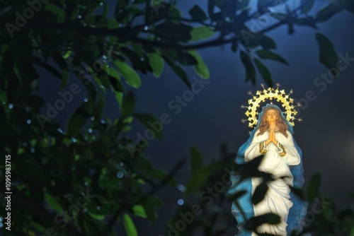 A large statue of the Assumption of Mary photographed from behind the trees at night photo