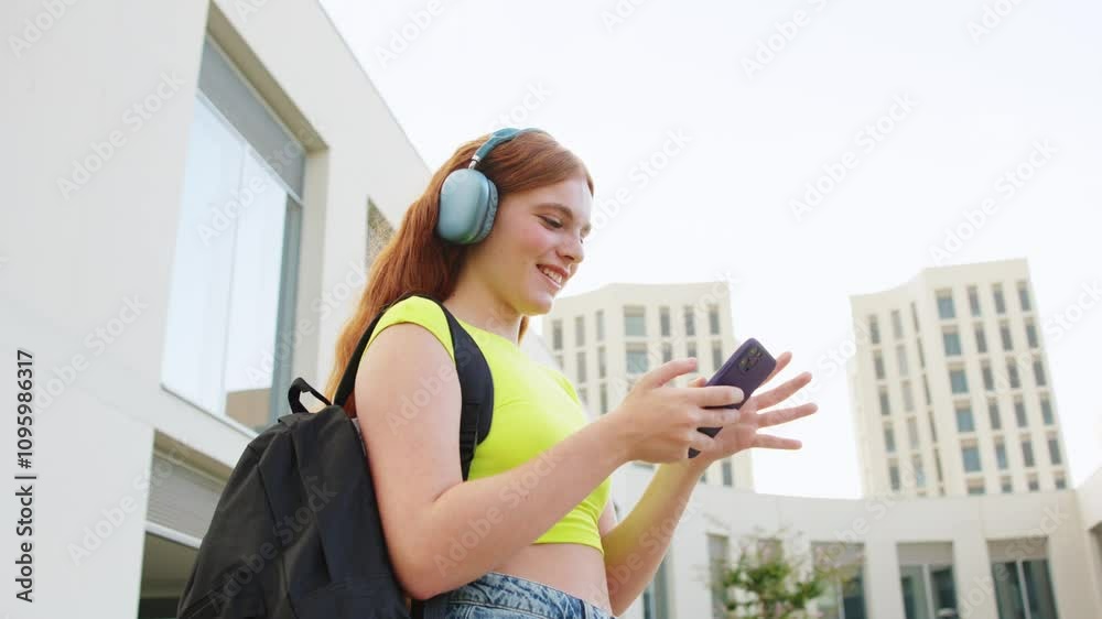 Student wearing headphones texting on smartphone Student wearing headphones texting on smartphone