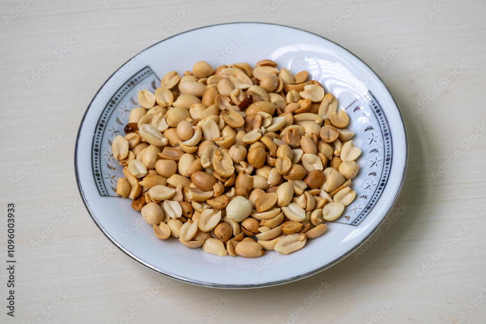 Roasted peanuts (Arachis hypogaea) on a white plate on a light wooden sruface. Roasted peanuts (Arachis hypogaea) on a white plate on a light wooden sruface.