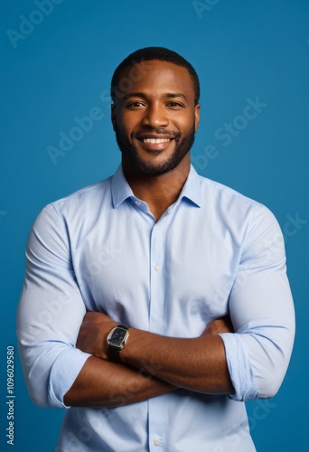 Professional headshot, smiling African American man, light blue button-down shirt, arms crossed, confident pose, warm expression, blue background, studio lighting, crisp and clear, positive energy, ap