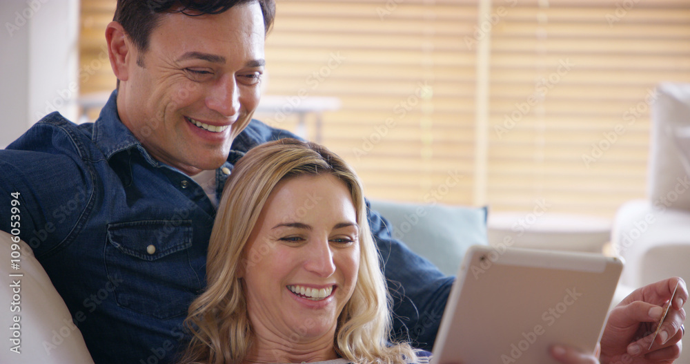 Happy, couple and tablet on sofa in home with streaming, series and technology with smile from meme. Internet, watching and love of people with app, online and fun together on weekend with care Happy, couple and tablet on sofa in home with streaming, series and technology with smile from meme. Internet, watching and love of people with app, online and fun together on weekend with care