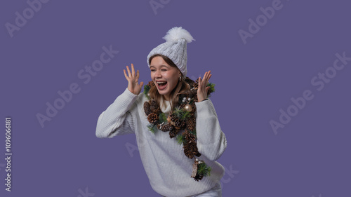 Cheerful young woman in white clothing and knitted hat excitedly screams surprised holding hands up, isolated on purple studio background. Middle shot photo