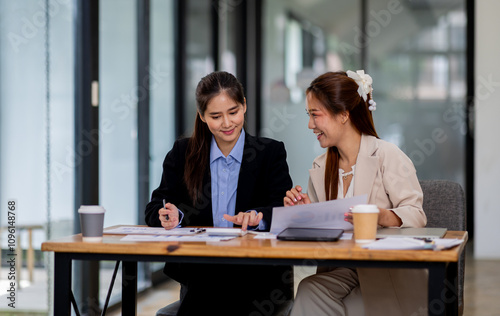 Two asian business women discuss financial management planning.standing and talking about analyzing documents in the workplace office 