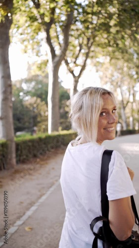 Young woman walking through a sunlit park, enjoying a leisurely stroll amidst trees and vibrant summer nature