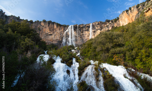 Fototapeta Naklejka Na Ścianę i Meble -  Scenic view of a waterfall flowing down a rocky cliff surrounded by a dense forest, creating a breathtaking natural landscape