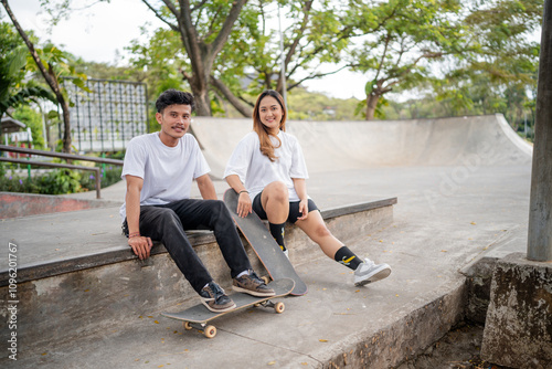 Two good friends are relaxing together on a skateboard ramp in a warm, sunny, beautiful park area