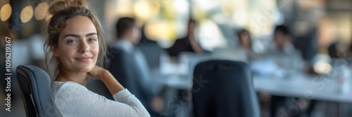 A woman smiles in a modern office setting, with colleagues in the background.