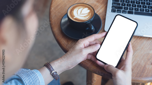 Cell phone white screen mockup, Woman hand holding mobile phone with blank screen while working at coffee shop. Business woman using smartphone, mockup for social media advertisement